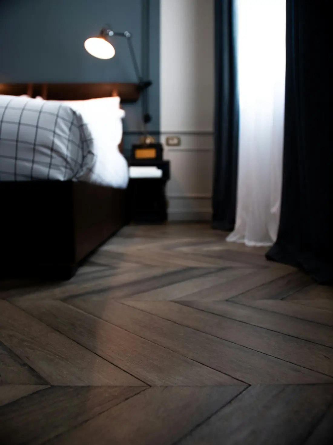 Chambre à la lumière tamisée, parquet sombre au pied du lit