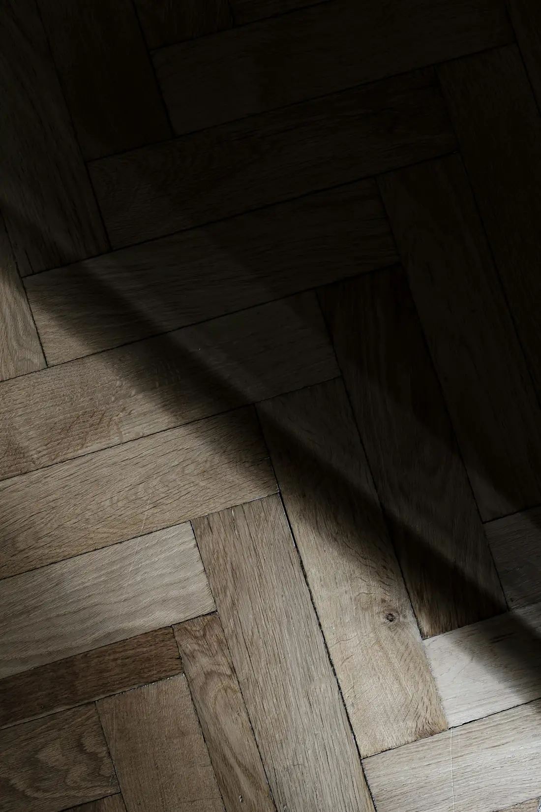 Parquet en bois dans la pénombre, traversé par la lumière d’une fenêtre