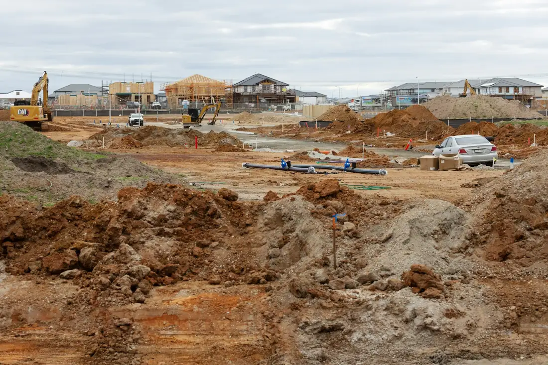 Terrain décapé, déblais et tuyaux posés au fond des tranchées, maisons en arrière-plan