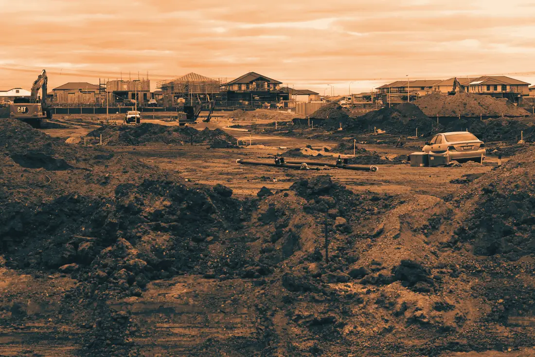 Terrain décapé, déblais et tuyaux posés au fond des tranchées, maisons en arrière-plan